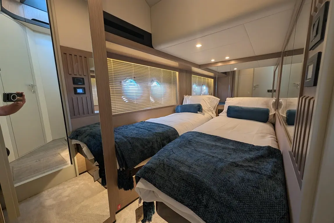 Luxurious twin bedroom featuring light wood accents, blue throws, a mirror, and a door to an adjoining bathroom.